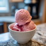 Two scoops of homemade Strawberry Banana Ice Cream in a white bowl on a granite countertop.
