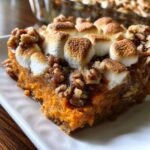 A close-up of a slice of sweet potato casserole topped with toasted marshmallows and chopped nuts.