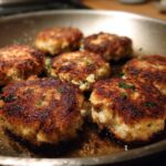 Close-up of several golden brown tuna cakes sizzling in a pan with a hint of parsley.