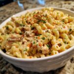 A close-up of creamy tuna macaroni salad in a white bowl, garnished with parsley and spices.