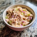 A close-up of a creamy tuna salad recipe with chunks of tuna, celery, and red onion in a light-colored bowl.