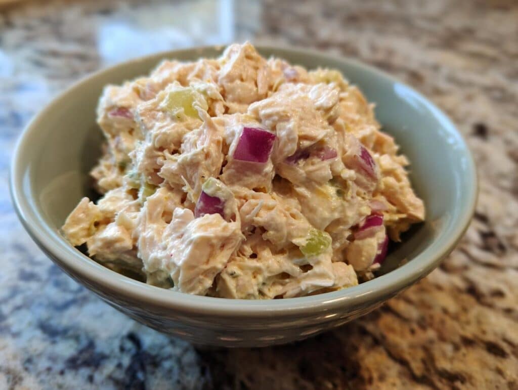 Close-up of a bowl filled with creamy tuna salad recipe, featuring chunks of tuna, red onion, and celery.