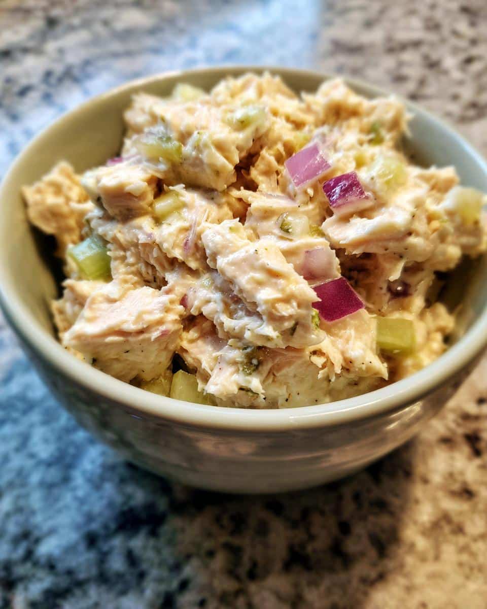 Close-up of a bowl filled with a creamy tuna salad recipe, featuring chunks of tuna, red onion, and celery.