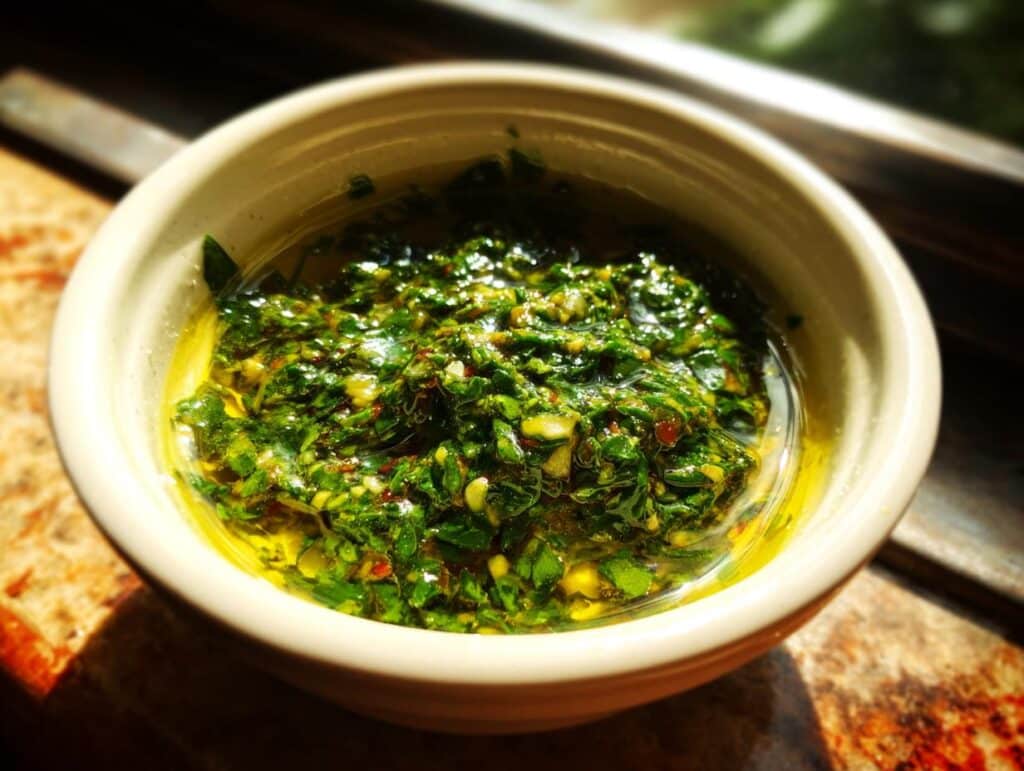 Close-up of vibrant green Chimichurri Sauce in a white bowl, showcasing its fresh herbs and olive oil.