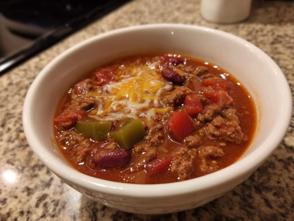 A bowl of taco soup filled with ground beef, tomatoes, beans, green peppers, and topped with melted cheese.