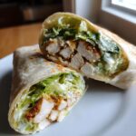 A halved chicken caesar wrap showing the filling of chicken, lettuce, and caesar dressing.