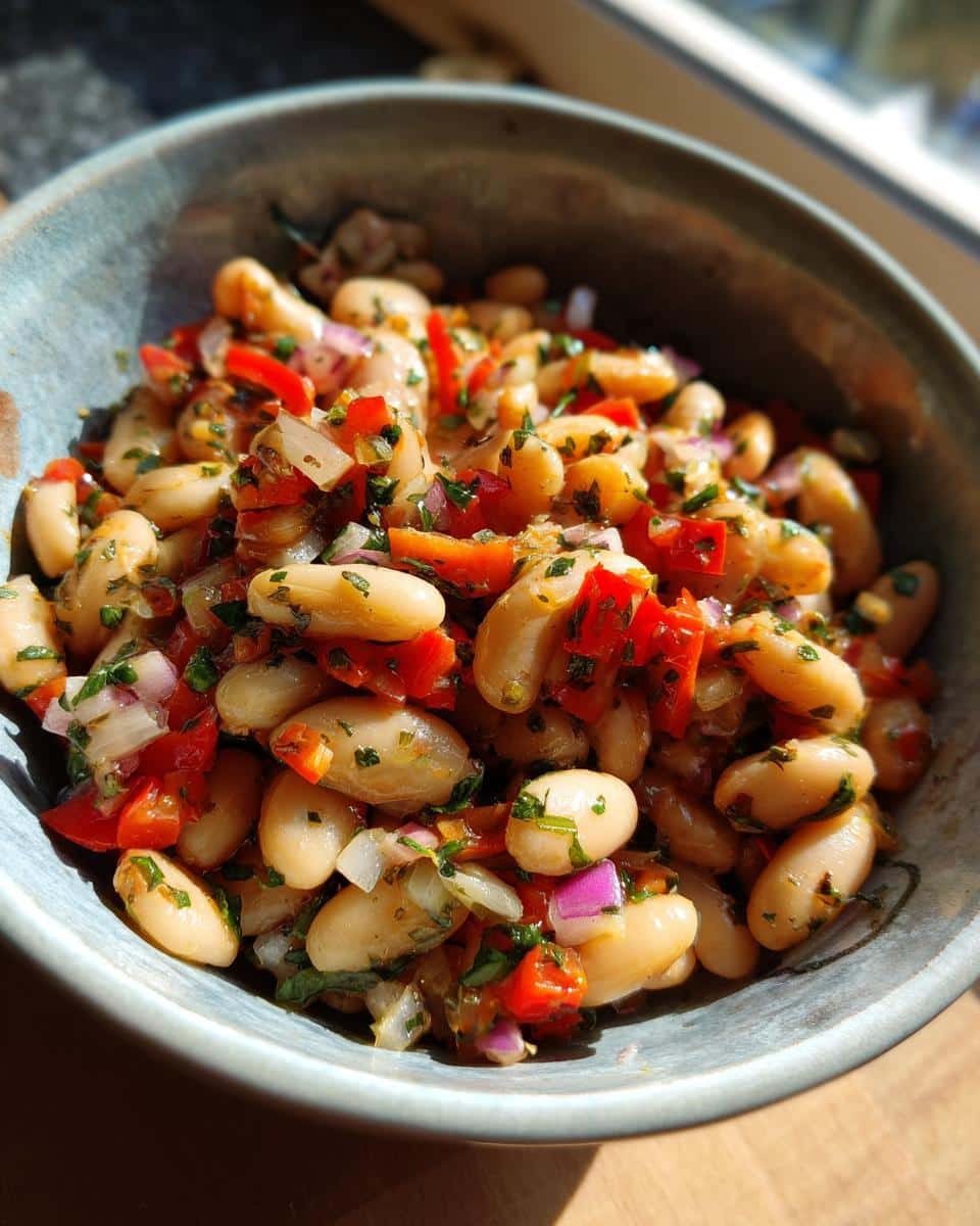 A bowl of fresh Dense Bean Salad with white beans, red bell peppers, red onions, and herbs.