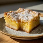 A single slice of lemon bars 9x13 pan, dusted with powdered sugar, sits on a plate.