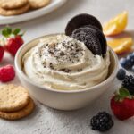 Bowl of Oreo sweet dip for parties, garnished with cookies and surrounded by fresh berries and cookies.