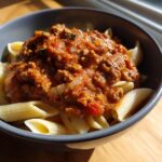Bowl of penne pasta topped with a rich tomato sauce featuring ground sausage recipes.