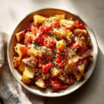 Bowl of roasted potatoes and tomatoes, garnished with herbs and cheese. Food babe recipe.