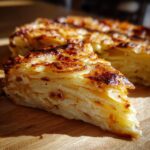 A slice of golden brown scalloped potatoes with visible layers, sitting on a wooden board.