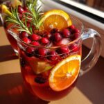 Pitcher of winter mocktails non alcoholic with cranberries, orange slices, lime, and rosemary garnish.