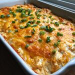 Close-up of a hot, bubbly buffalo chicken dip canned chicken, topped with melted cheddar cheese and fresh green onions in a white baking dish.