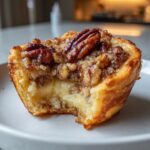 A close-up shot of a pecan tassie with a bite taken out, revealing the creamy filling and crunchy pecan topping.