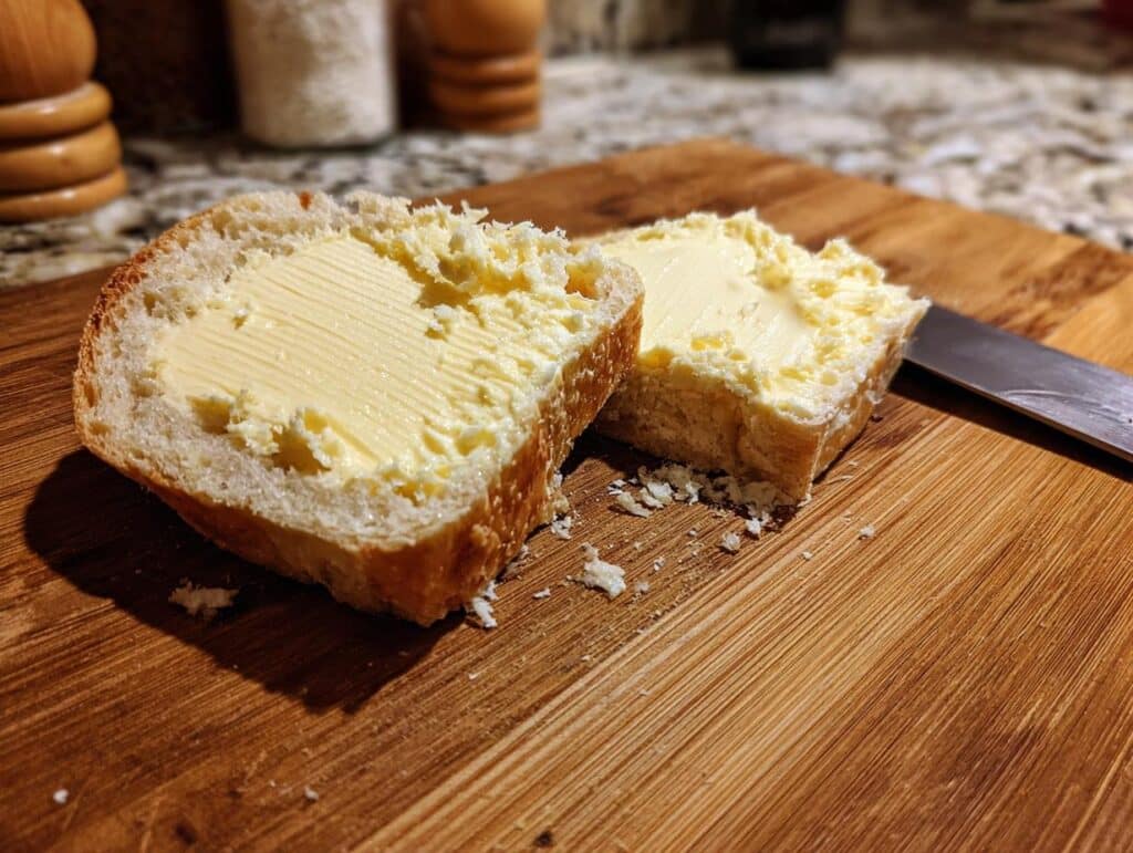 Two slices of bread generously spread with butter on a wooden butter board, ready to eat.