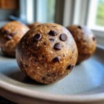 A close-up of a single Chocolate Chip Cookie Dough Protein Ball on a plate, showing texture and chocolate chips.