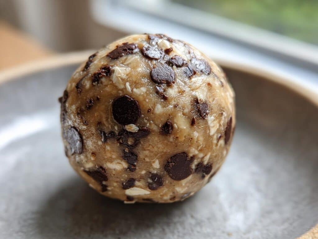 A single Chocolate Chip Cookie Dough Protein Ball, rich with chocolate chips and oats, resting on a gray plate.