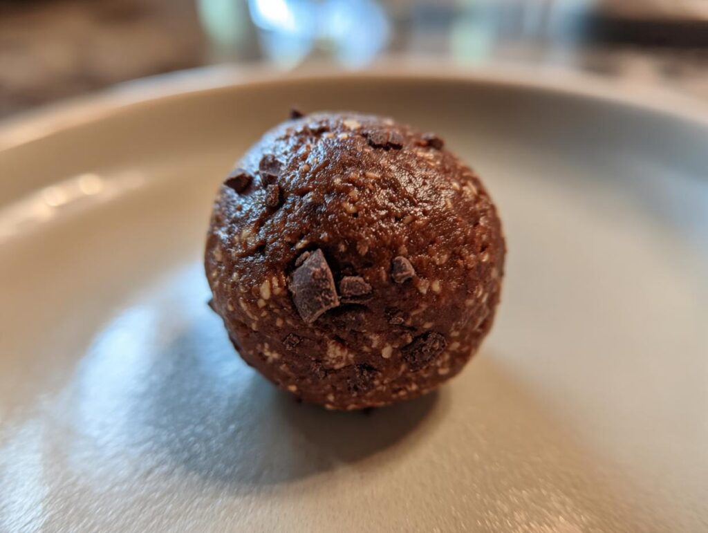 A single, round Chocolate Mint Protein Bite on a light-colored plate, speckled with chocolate chips.