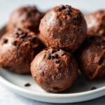 A close-up shot of several round Chocolate Mint Protein Bites, topped with mini chocolate chips, on a light gray plate.
