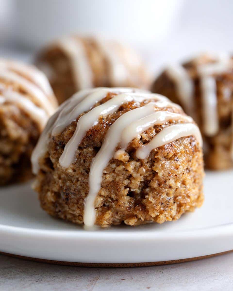 A close-up shot of a single Cinnamon Roll Protein Bite, drizzled with white icing, on a white plate.