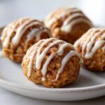 Four round Cinnamon Roll Protein Bites drizzled with white icing on a light-colored plate.