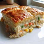 A close-up of a golden-brown slice of Creamy Chicken Pot Pie Casserole with flaky pastry crust and creamy filling.