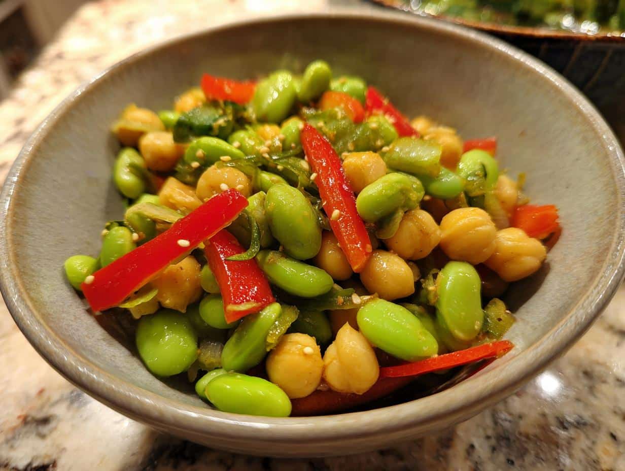 Close-up of a vibrant Edamame Chickpea Salad with red bell pepper strips and sesame seeds in a gray bowl.