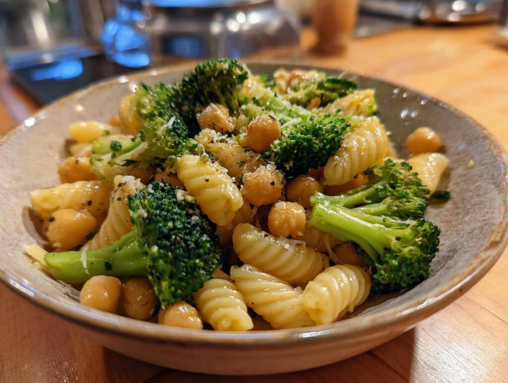 A close-up of a bowl of Garlic Olive Oil Broccoli Chickpea Pasta, garnished with cheese and pepper.