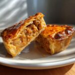 A close-up shot of a gluten free mini tourtiere cut in half, revealing the savory meat filling and golden-brown crust.