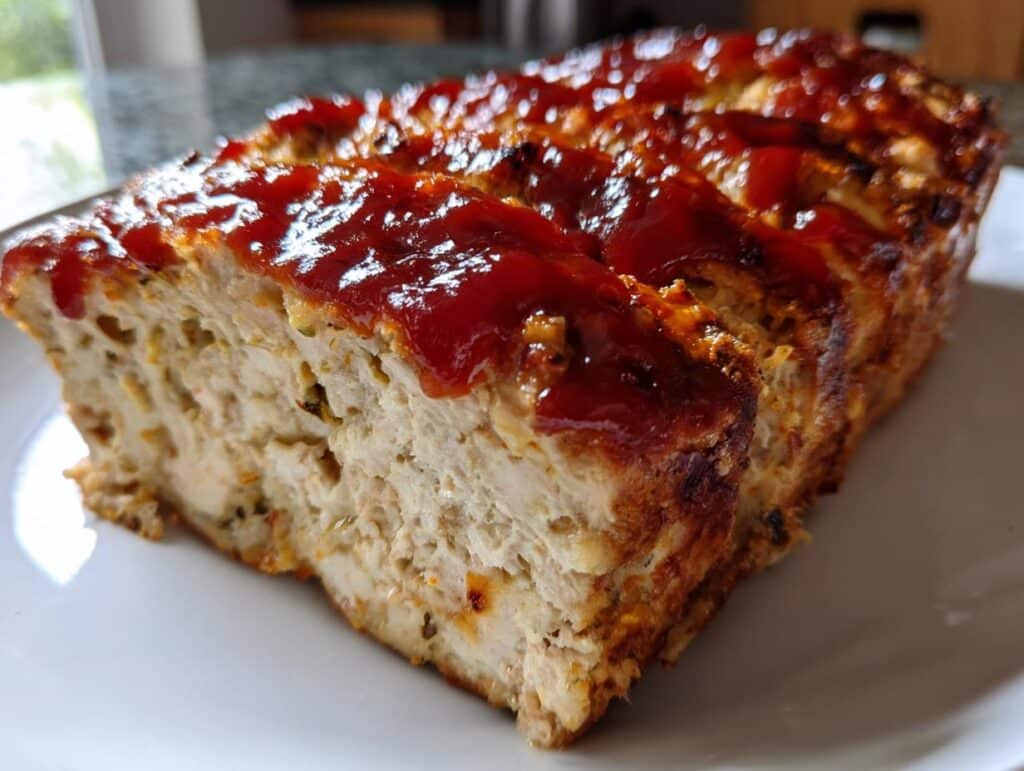 A close-up shot of a baked loaf of Juicy Garlic Parmesan Chicken Meatloaf with a glistening red glaze on top.