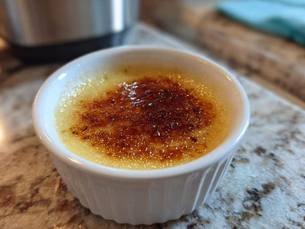 A single serving of Lemon Brûlée Posset in a white ramekin, showcasing the caramelized sugar crust.
