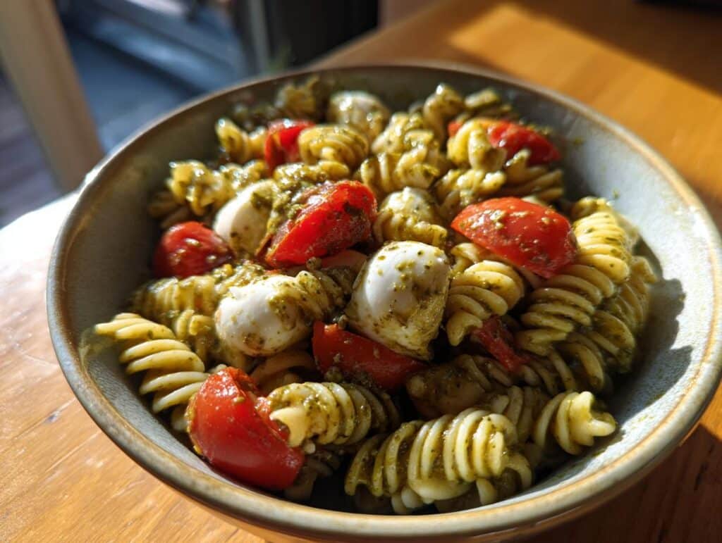 Close-up of a bowl of Light & Creamy Pesto Caprese Pasta Salad with fusilli, cherry tomatoes, and mozzarella.