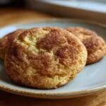 Close-up of two golden-brown snickerdoodle cookies recipe on a light blue plate, dusted with cinnamon sugar.