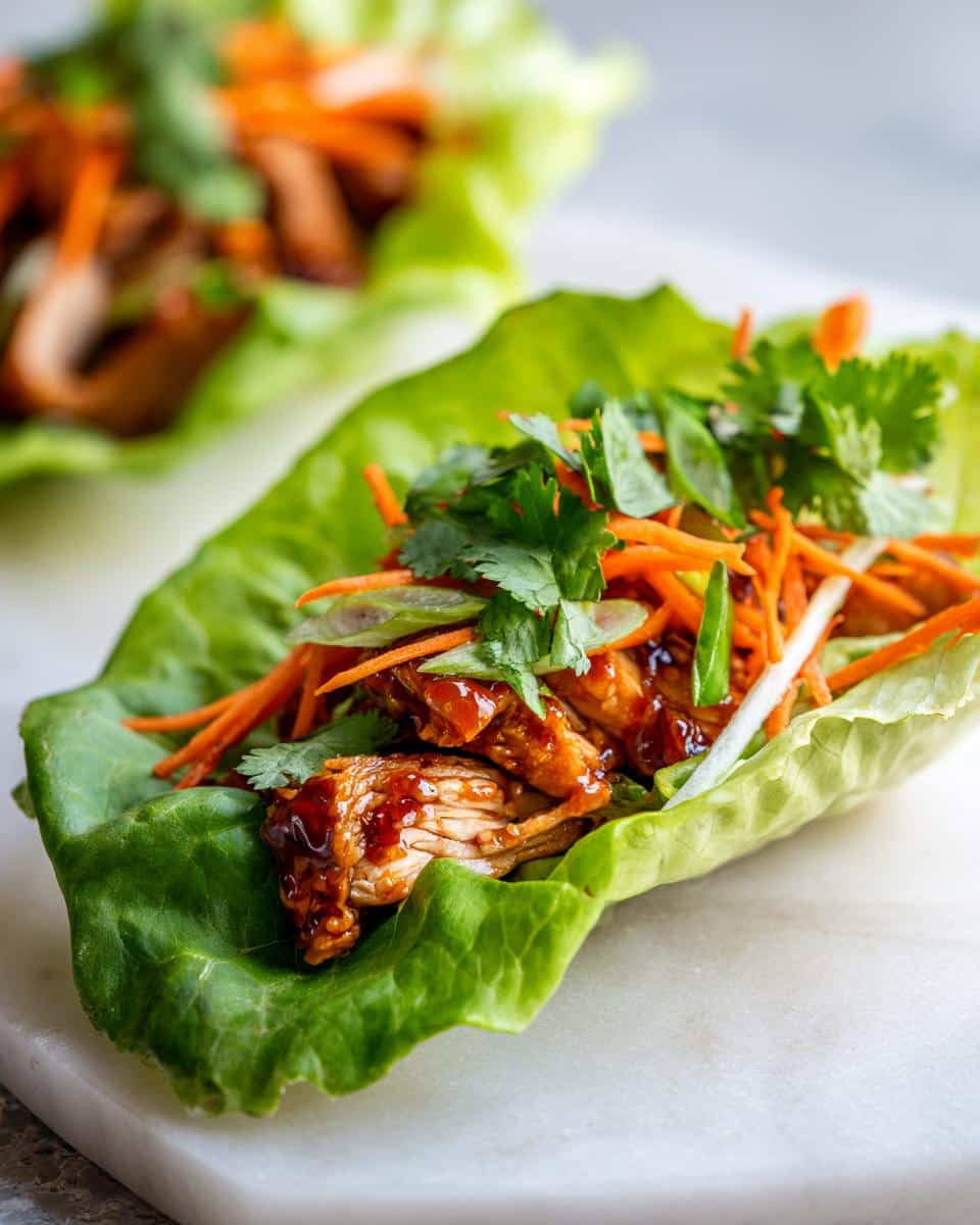 Close-up of a Sweet Chili Chicken Wrap filled with shredded chicken, carrots, green onions, and cilantro.