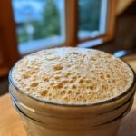 Close-up of a jar filled with bubbly active sourdough starter, showing its foamy texture and readiness for baking.