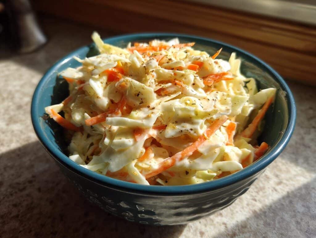 A bowl of coleslaw featuring shredded cabbage, carrots, and a creamy coleslaw dressing, ready to serve.