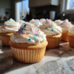 Close-up of bridal shower cupcakes topped with white frosting and pastel sprinkles.