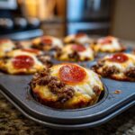 Close-up of Carnivore Pizza Muffins in a muffin tin, topped with cheese, ground meat, and pepperoni.