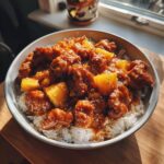 Bowl of chicken pineapple recipe served over rice, garnished with sesame seeds.