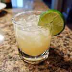 A glass of best classic margarita recipe with ice, a salted rim, and a lime wedge.