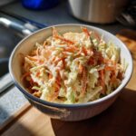 A bowl of coleslaw with creamy coleslaw dressing, shredded cabbage, and carrots, seasoned with pepper.