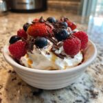 A bowl of fluffy yogurt topped with fresh raspberries, blueberries, strawberries, and chocolate shavings.