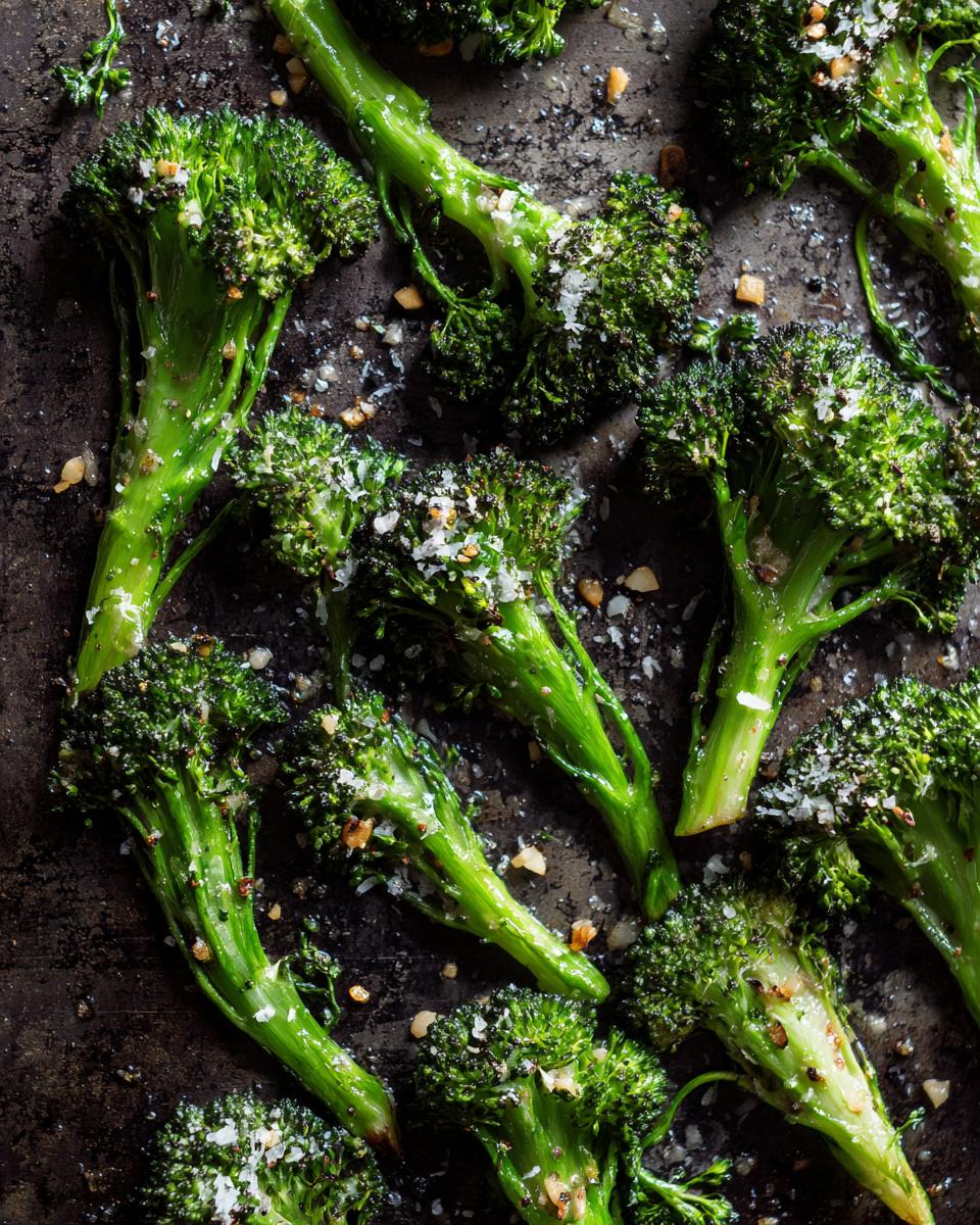 Overhead view of Garlic Parmesan Broccoli florets roasted on a dark baking sheet, seasoned with garlic and parmesan.