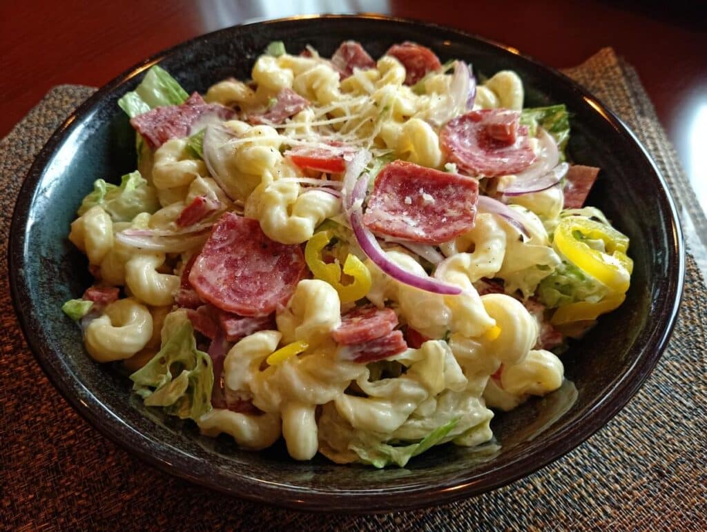 A bowl of creamy grinder pasta salad with elbow macaroni, salami, lettuce, onions, and peppers.