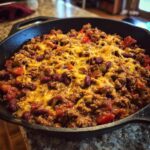 Skillet filled with a cheesy ground beef recipe, including ground beef, kidney beans, tomatoes, and melted cheese.