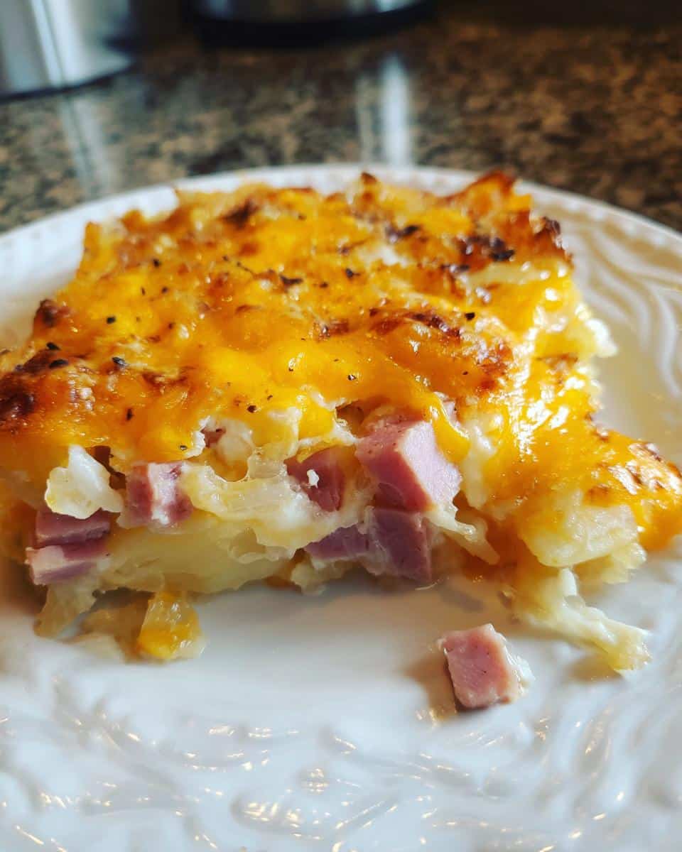 A slice of instant pot cheesy scalloped potatoes and ham on a white plate, showcasing the layers of potatoes, ham, and cheese.