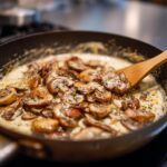 Close-up of Mushroom Cream Sauce being stirred in a pan with a wooden spoon.