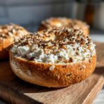 A protein bagel with greek yogurt and everything bagel seasoning on a wooden board. High protein snack.