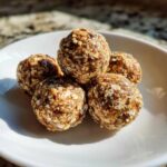 A stack of five homemade protein balls with protein powder on a white plate, ready to eat.